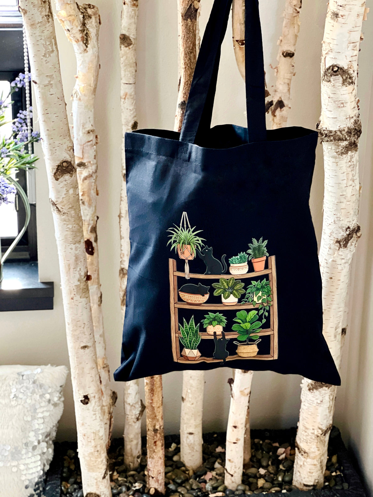 Black tote bag with plant design hanging on a tree