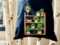 Black Cat Tote Bag with a wooden shelf design featuring plants and cats on a white background.