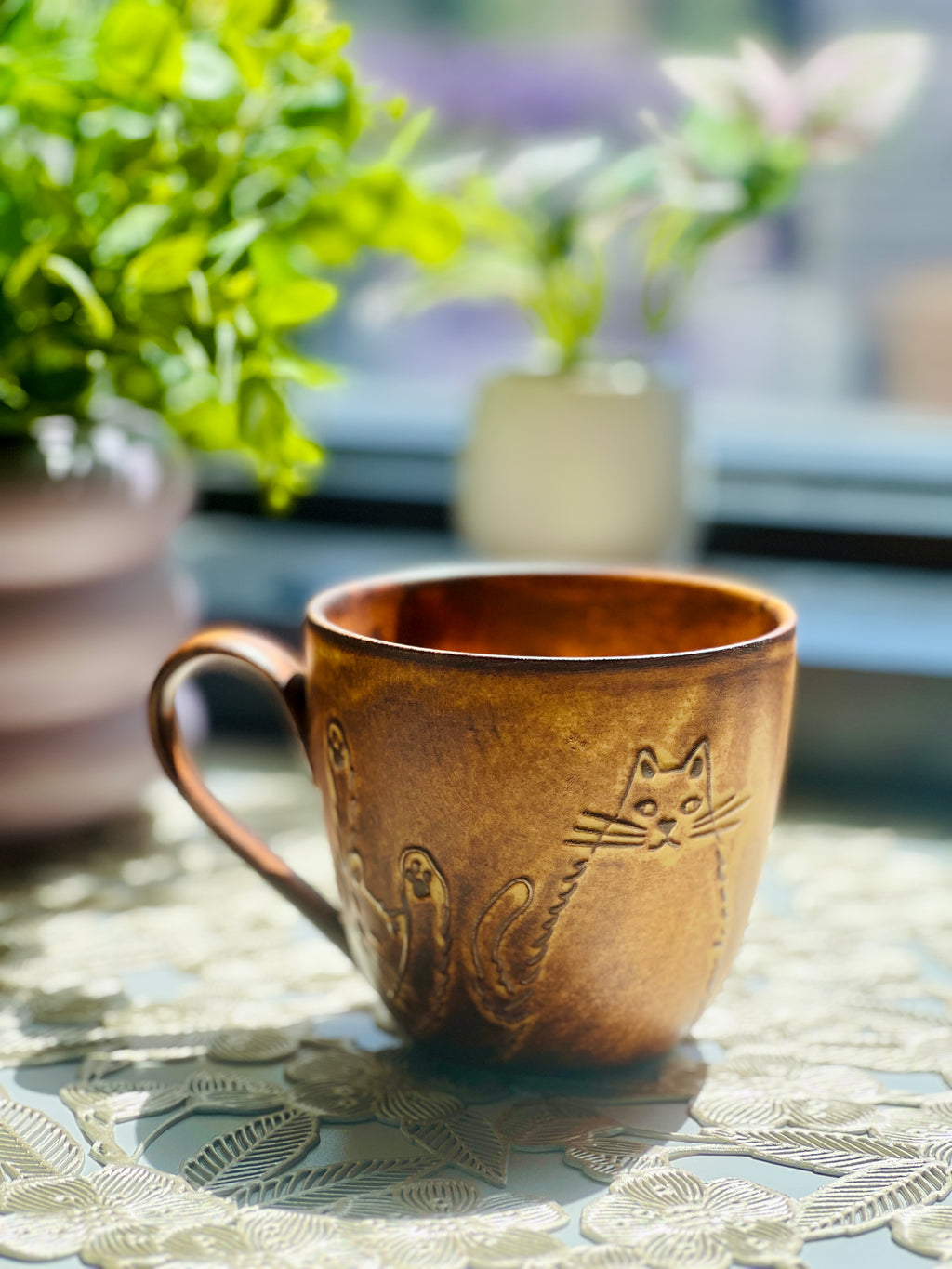 Brown ceramic mug with cat designs on a table outdoors