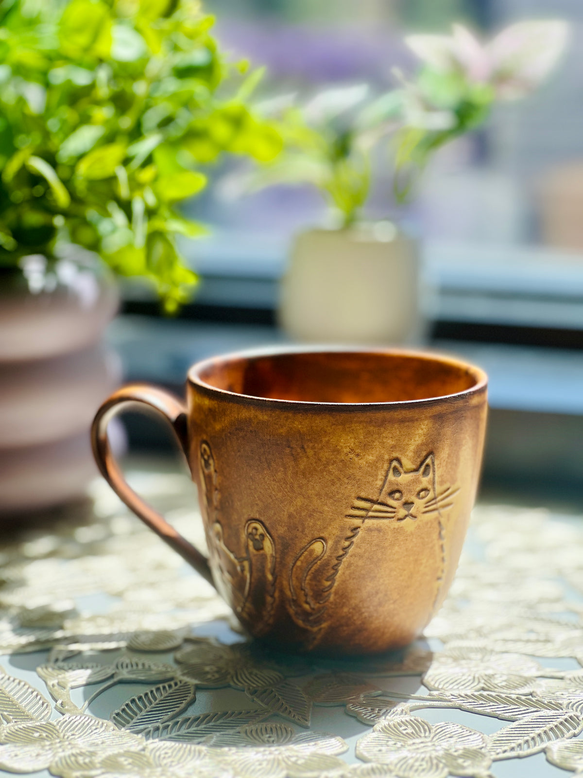 Brown ceramic mug with cat designs on a table outdoors