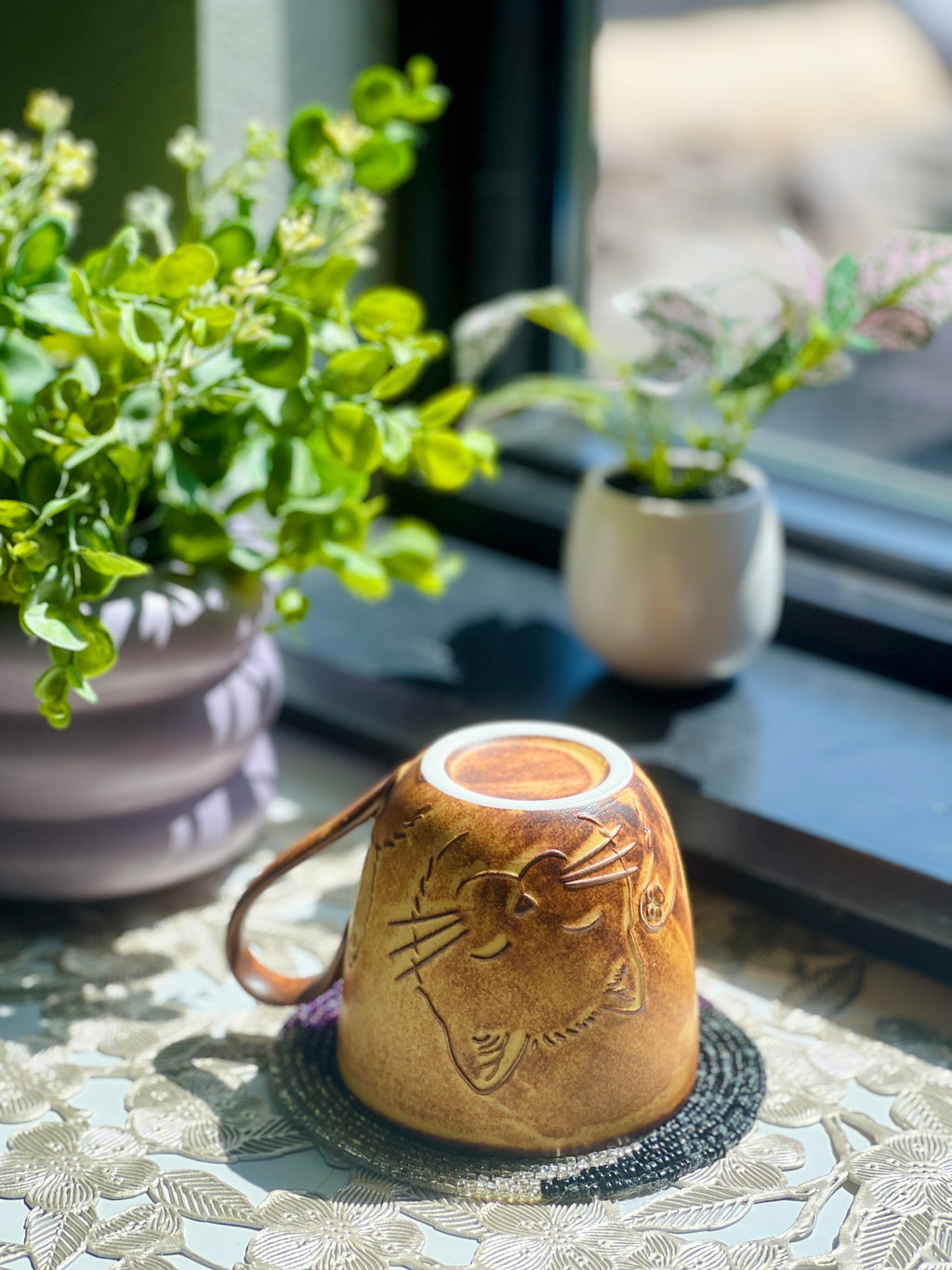 Ceramic mug with cat design on a table with plants in the background