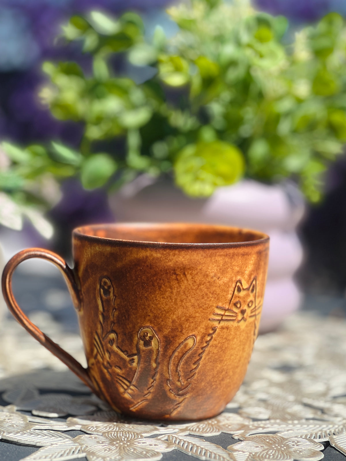 Brown ceramic mug with embossed design on a textured surface with greenery in the background