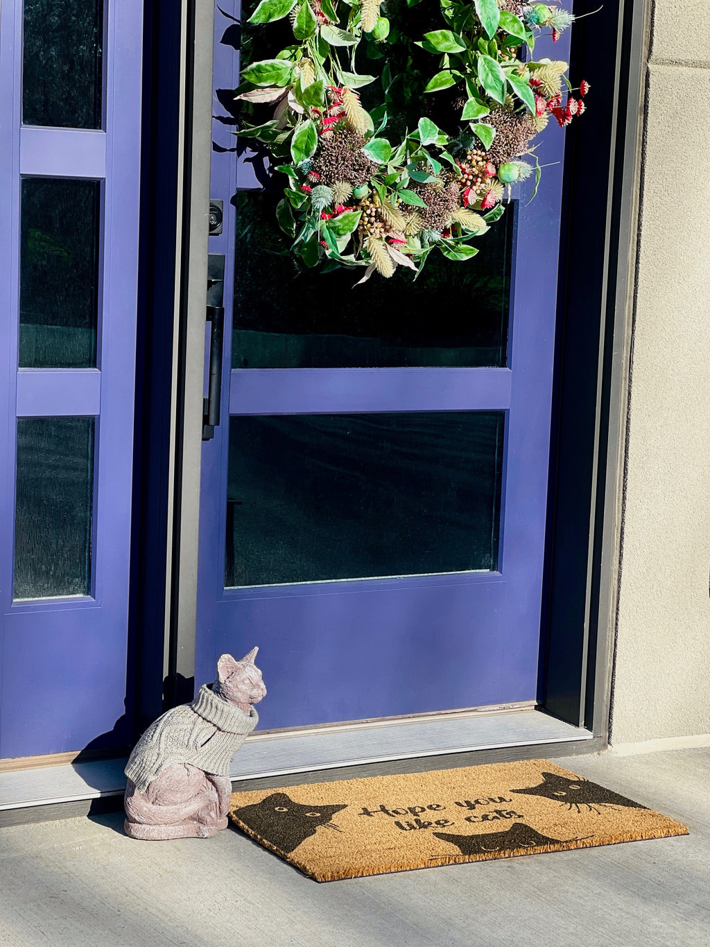 Purple door with a wreath, cat statue, and doormat on a porch.