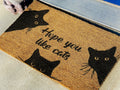 Doormat with black cat designs and text 'Hope you like cats' on a textured surface.