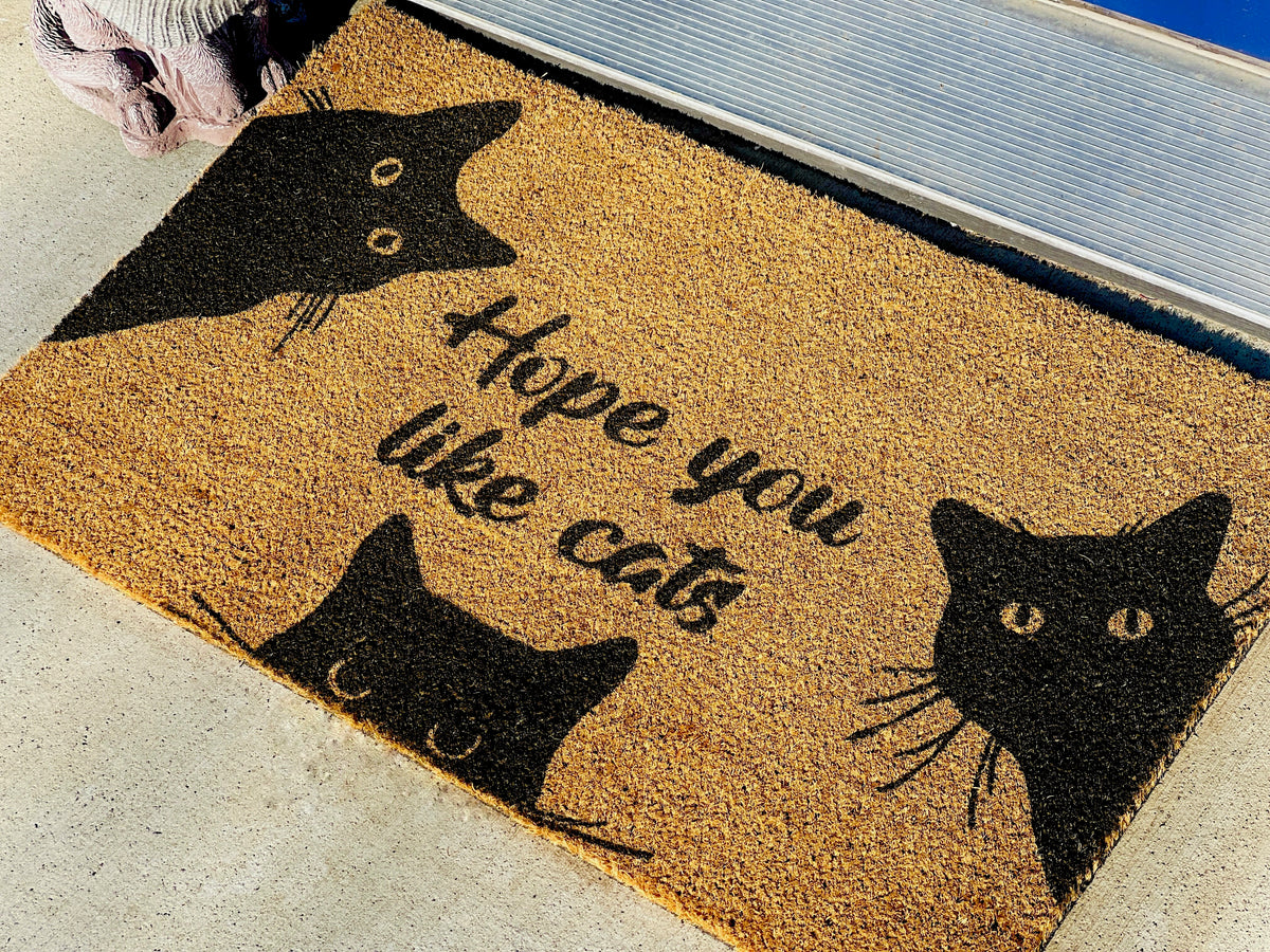 Doormat with black cat designs and text 'Hope you like cats' on a textured surface.