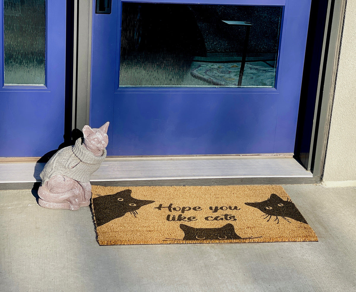 Cat statue on a doormat with cat-themed design and blue door in the background