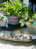 Decorative setting with a plate of stones, a gold rimmed bowl, and potted plants.