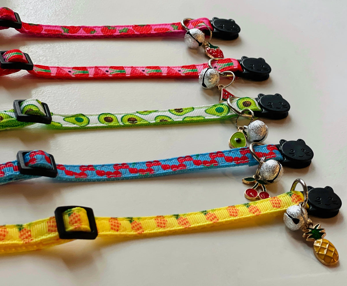Five colorful cat collars with decorative charms on a white surface