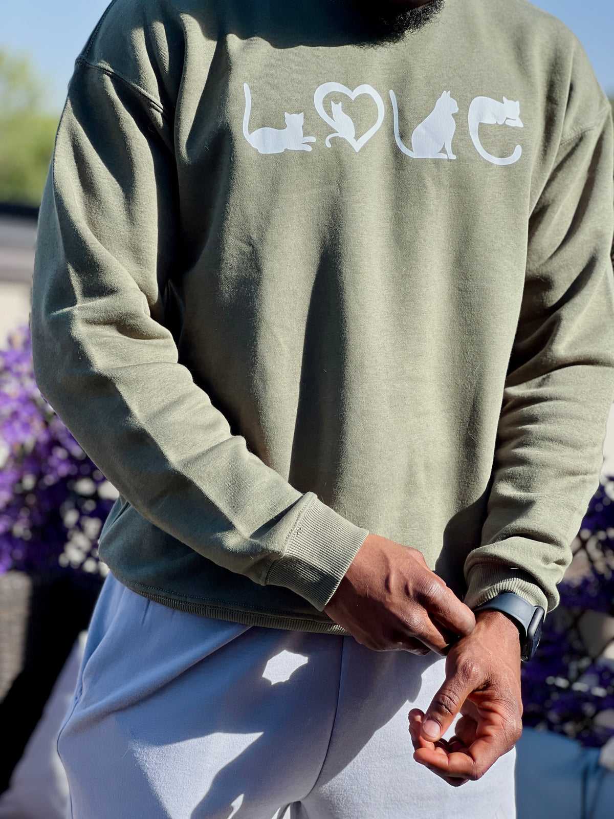 Person wearing a green sweatshirt with 'LOVE' and a heart design, standing outdoors.