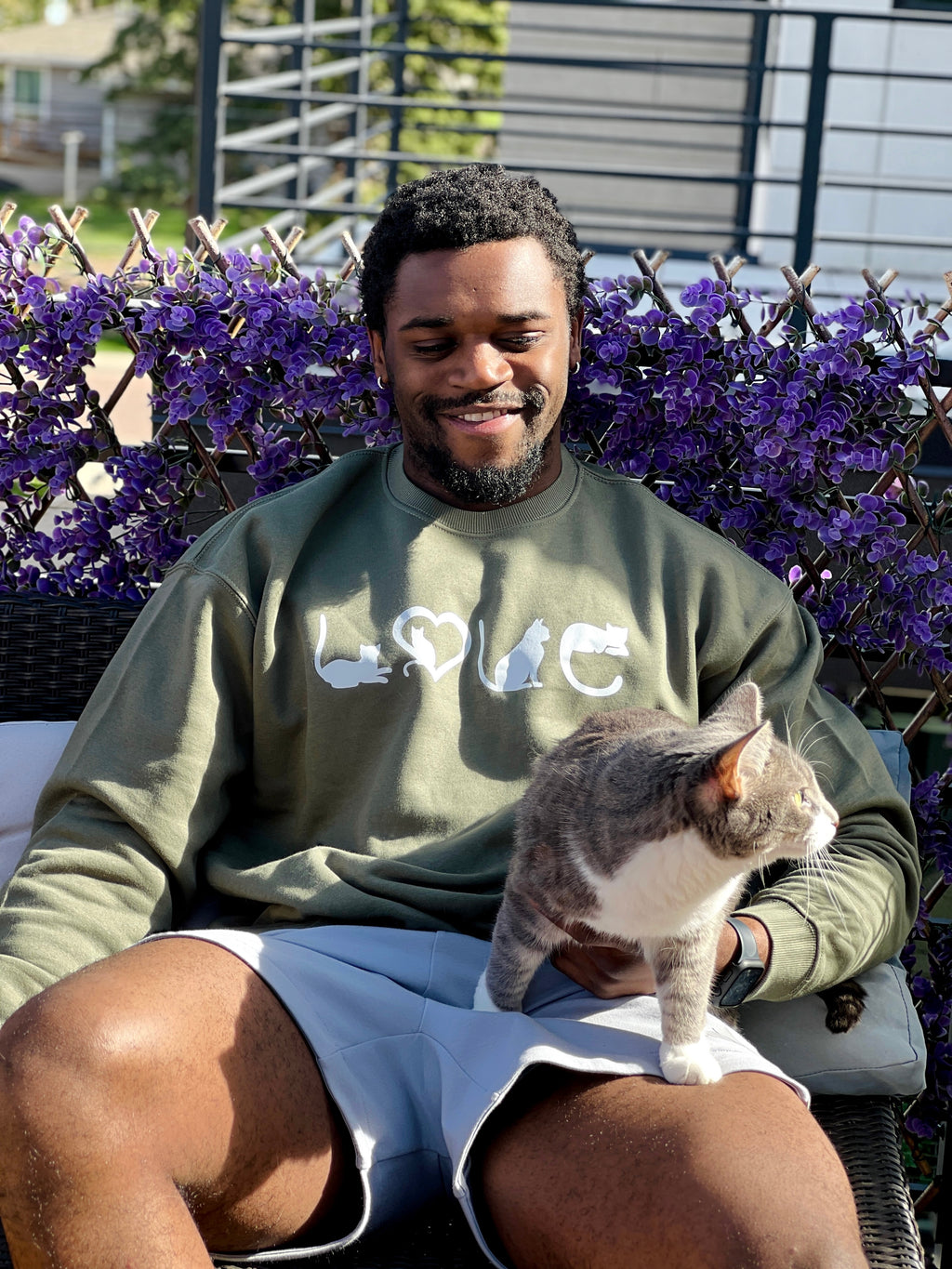 Man sitting outdoors with a cat on his lap, wearing a sweatshirt with 'LOVE' printed on it.