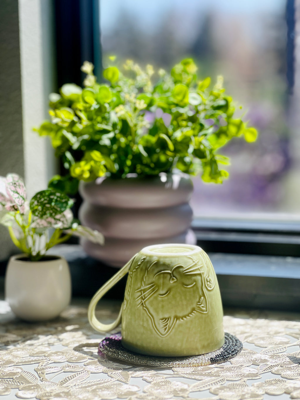 Green ceramic container with a decorative design on a stone surface with plants in the background.