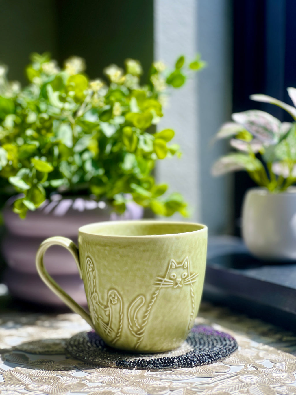 Green ceramic mug with cat design on a table with plants in the background