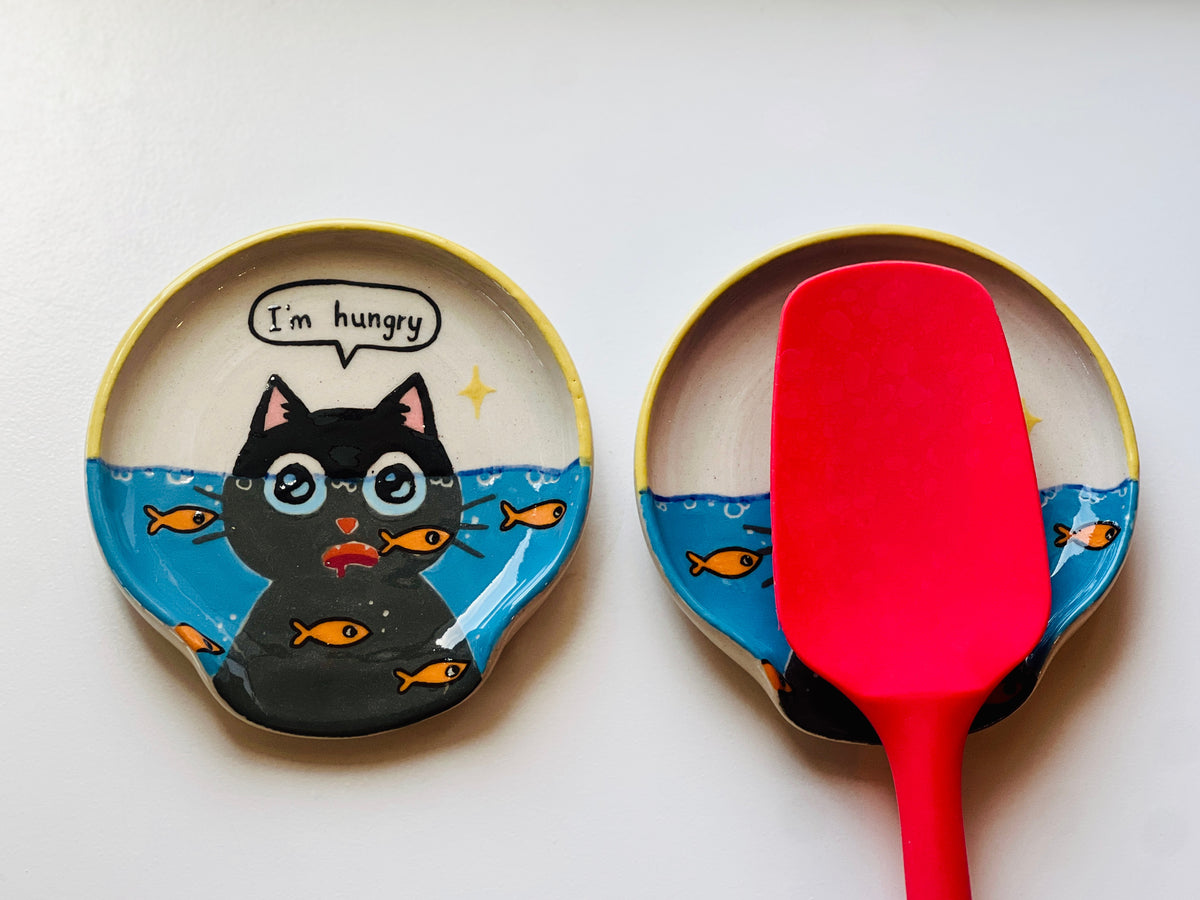 Two ceramic plates with a cat design and a red spatula on a white background