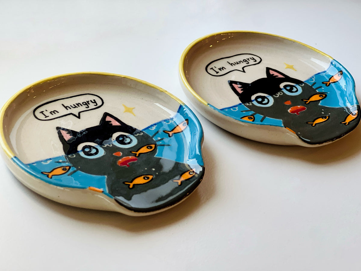 Two ceramic plates with cat illustrations and 'I'm hungry' text on a white background