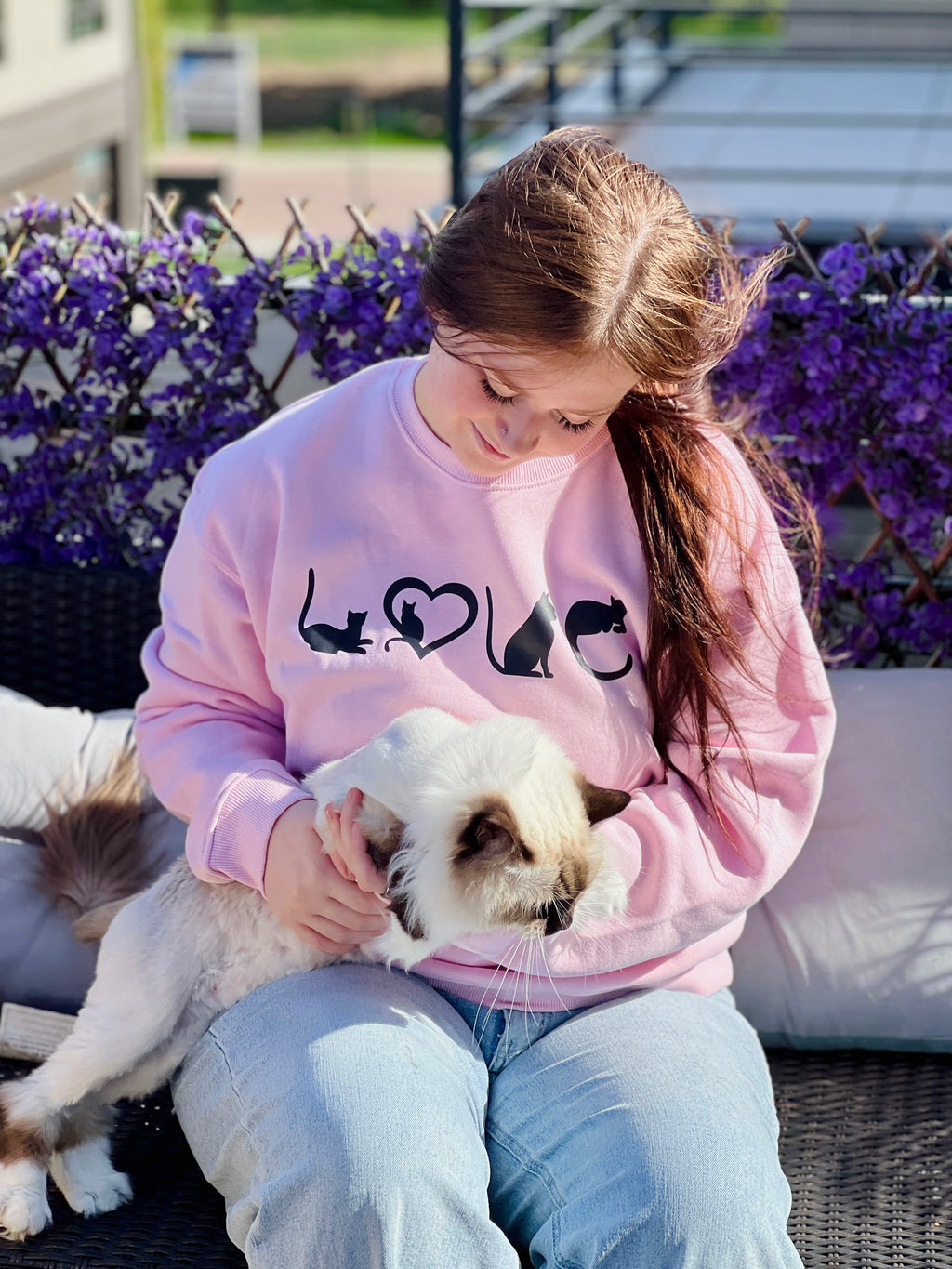 Person wearing a pink sweatshirt with 'LOVE' printed on it, sitting outdoors with a small dog.