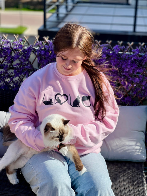 Person wearing a pink sweatshirt with cat  LOVE designs, sitting outdoors with a cat on their lap.