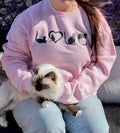 Person wearing a pink sweatshirt with cat designs holding a cat outdoors.