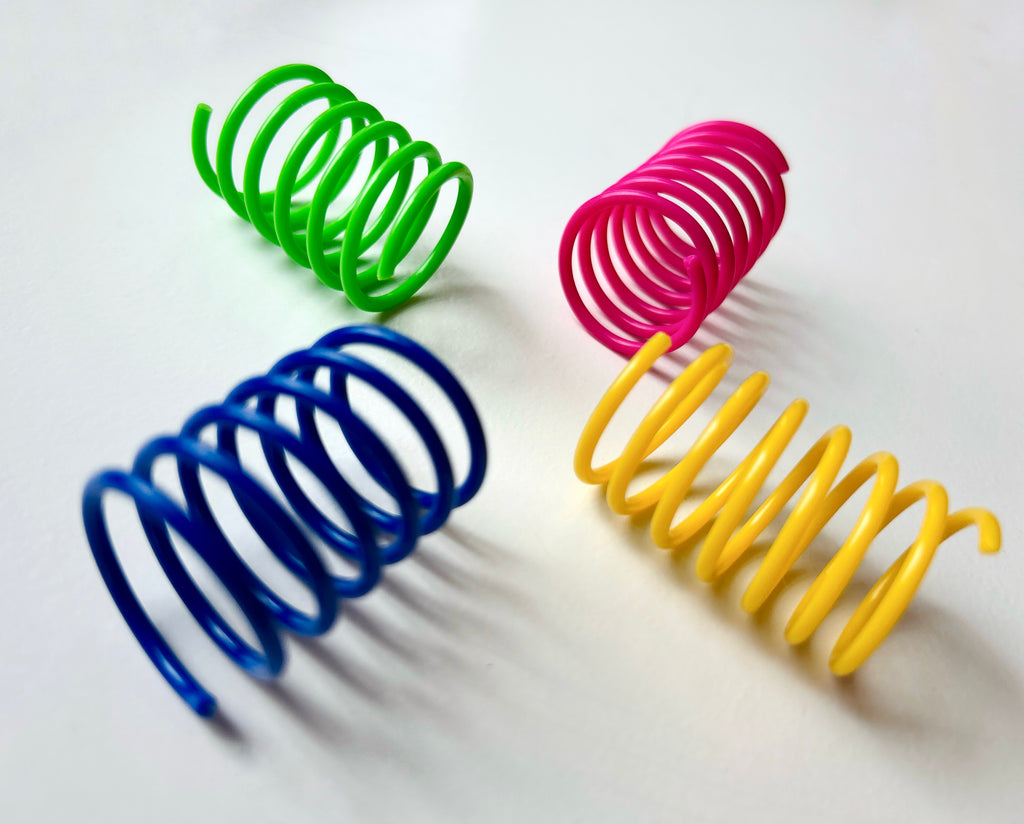 Four cat coil spring toys in green, blue, pink, and yellow arranged on a plain white background.