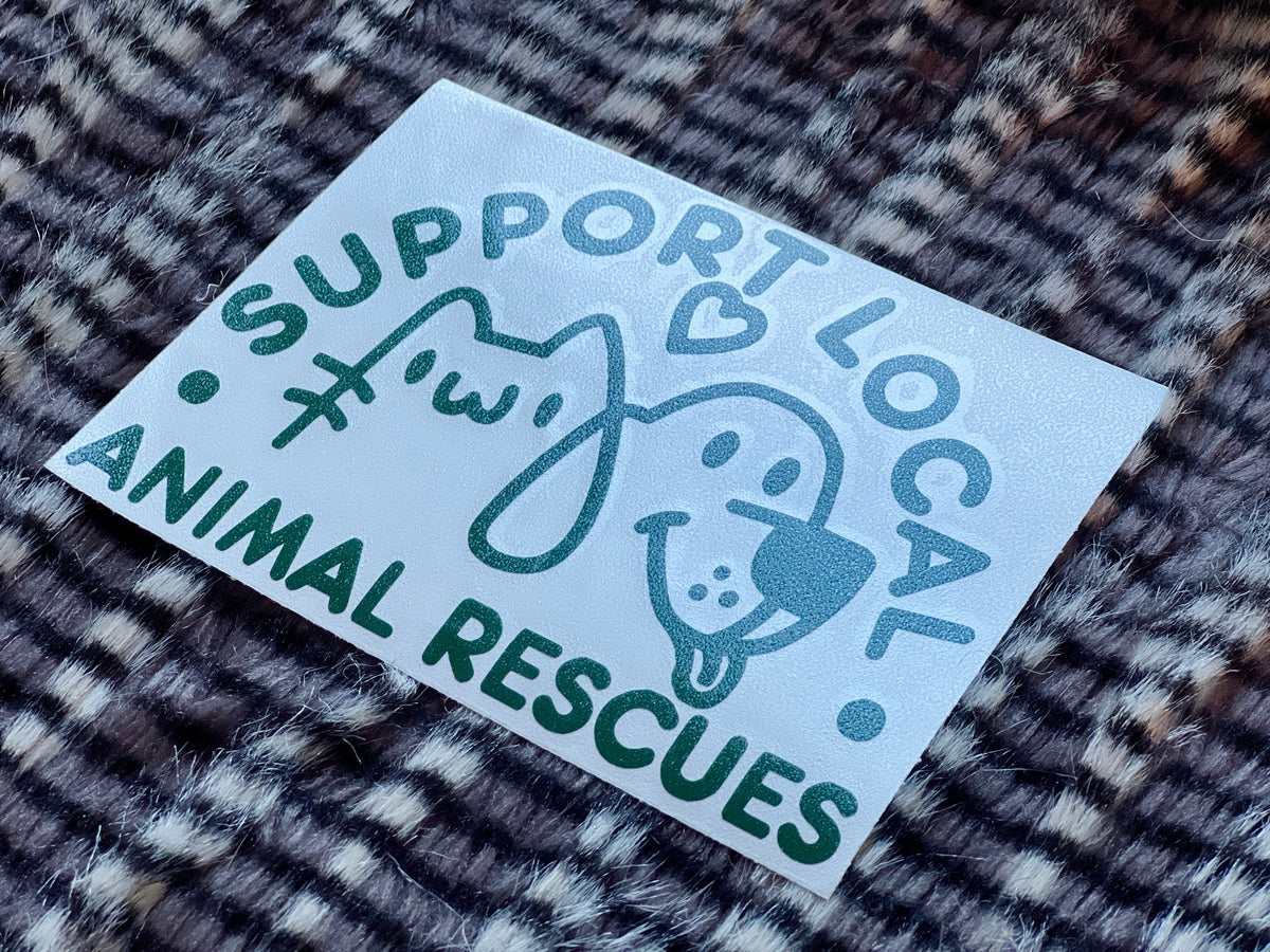 Green sticker with 'Support Local Animal Rescues' text and dog and cat illustrations on a textured surface.