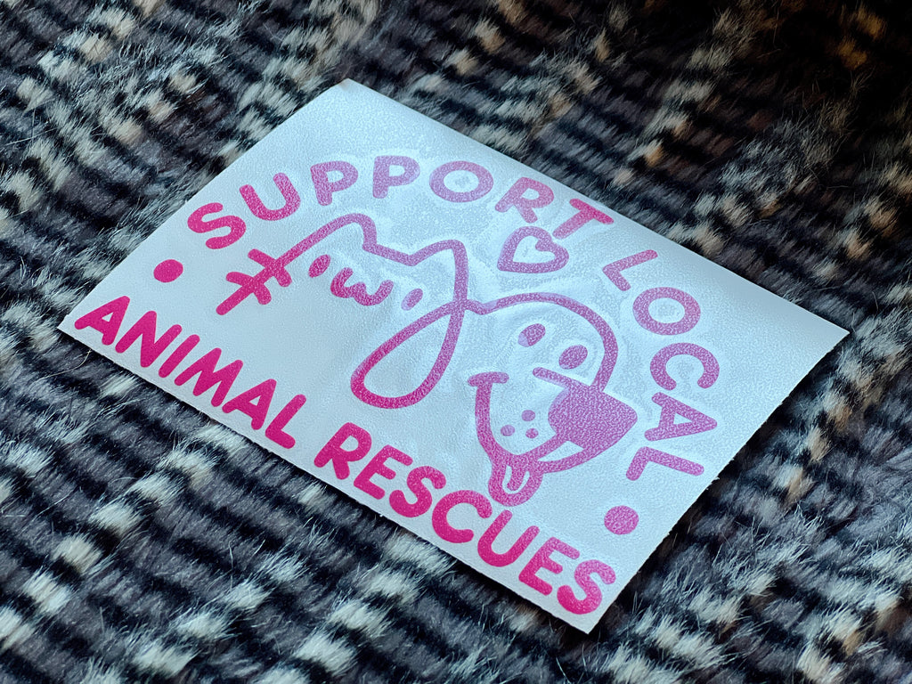 Pink sticker with text 'Support Local Animal Rescues' on a textured surface