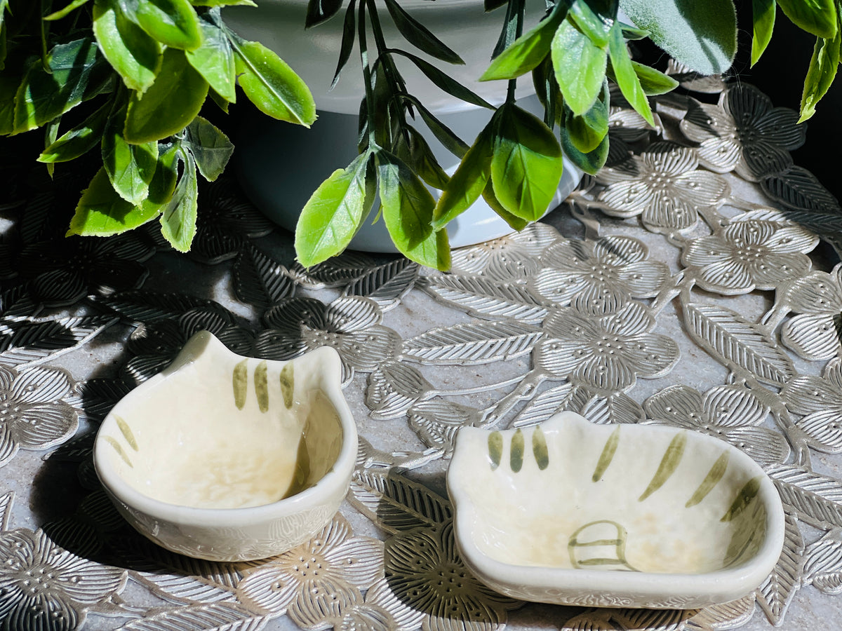 Two small ceramic bowls with leaf patterns on a textured surface with green leaves in the background.