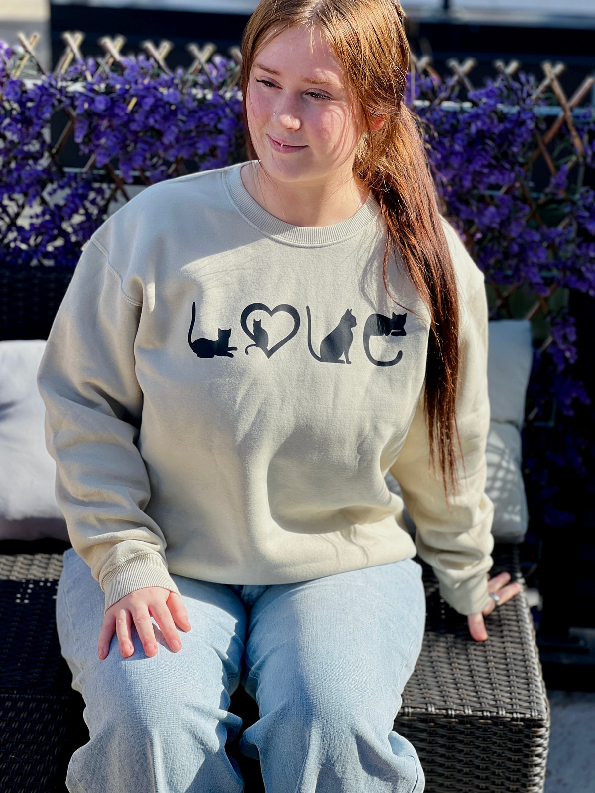Person wearing a tan sweatshirt with black text and cat graphics, sitting outdoors.