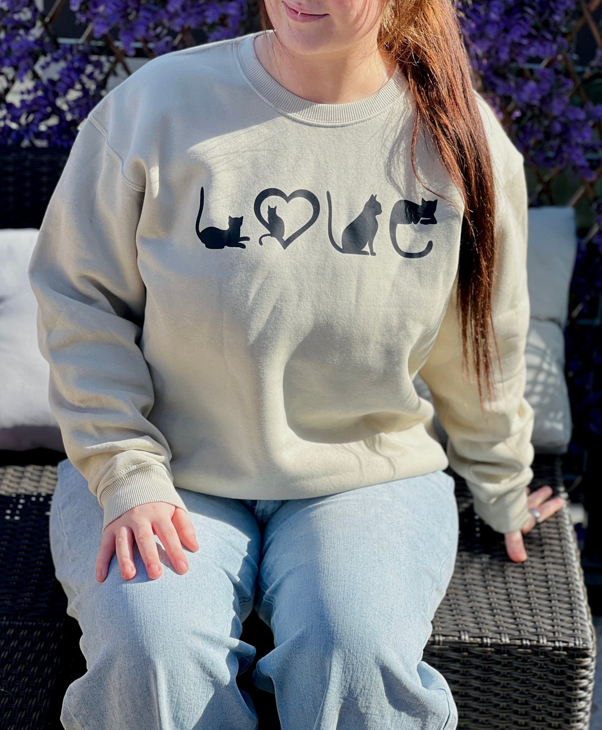 Person wearing a tan sweatshirt with cat designs and the word 'LOVE' sitting outdoors.