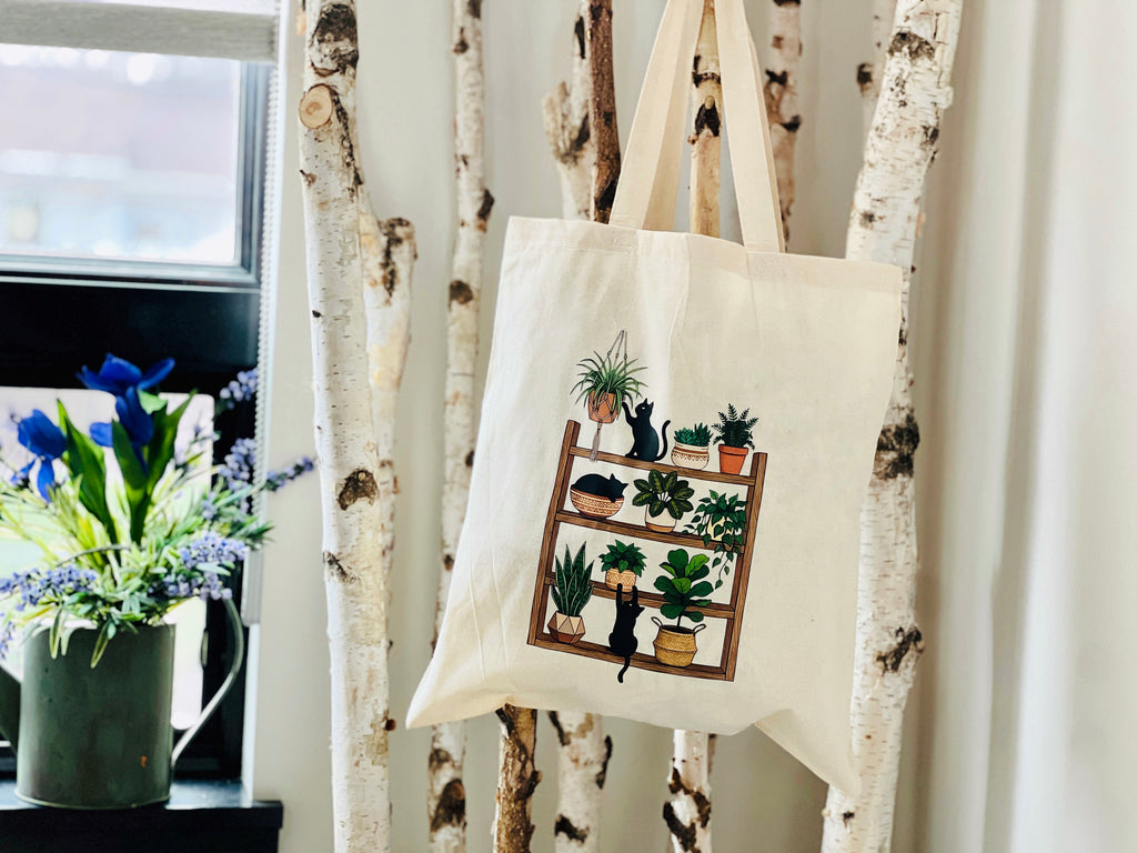 Tote bag with plant and cat design hanging on a decorative stand.