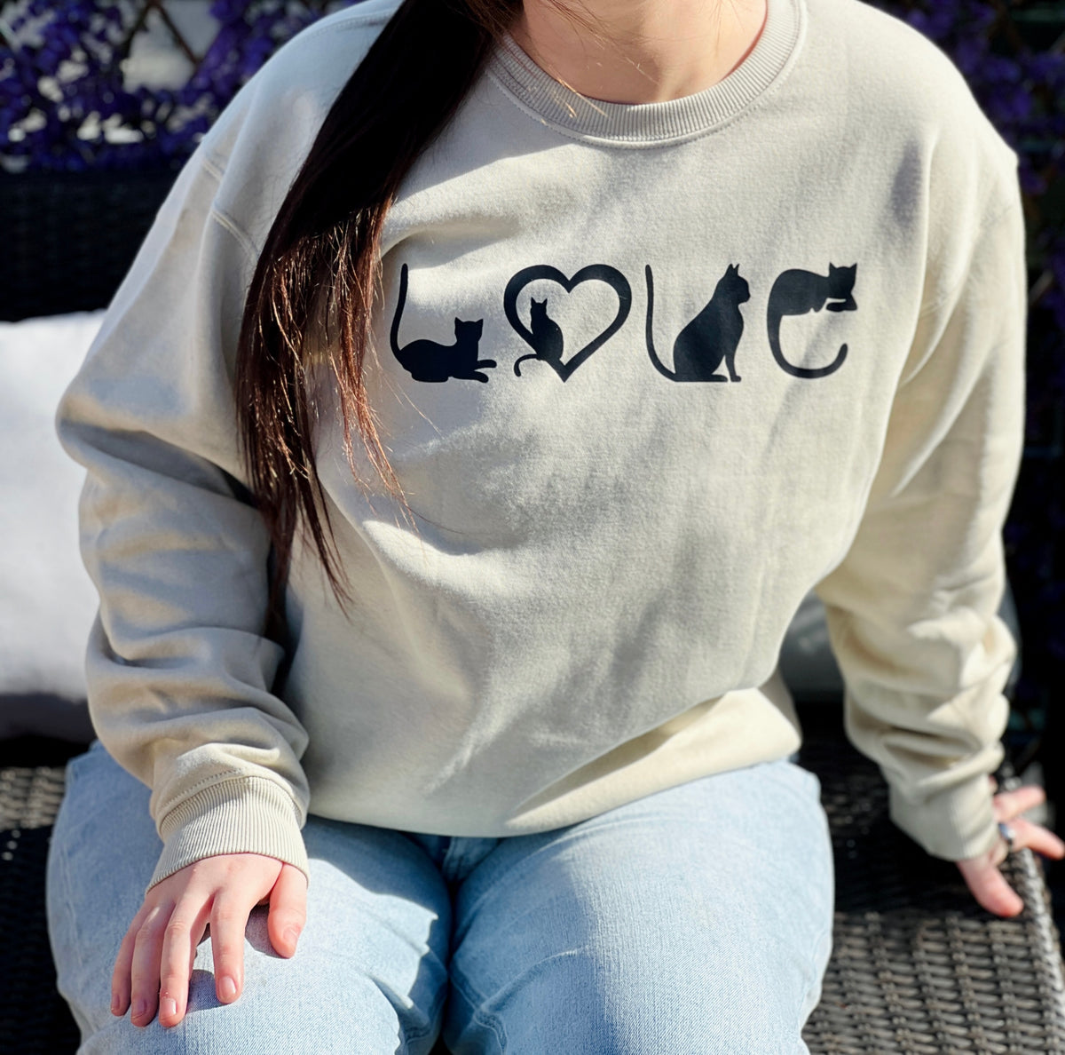 Person wearing a tan crewneck with black cat illustrations and 'LOVE' text.